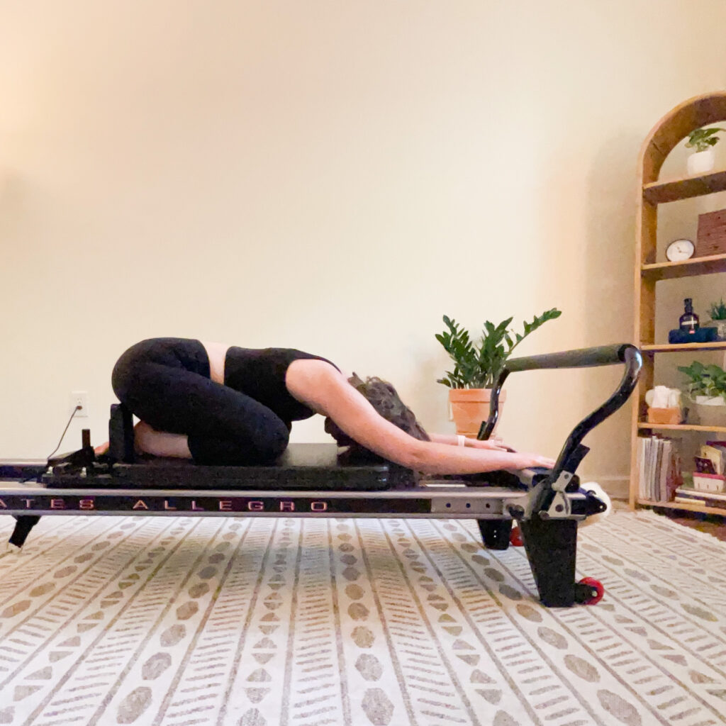 This image shows Allie, Pilates instructor and studio owner, resting in child's pose on top of a reformer.